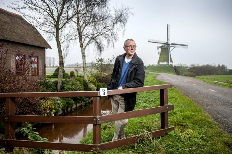 foto van een man die ontspannen tegen een hek aan leunt